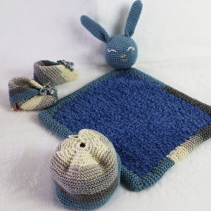 Un bonnet et des chaussons naissance 3/6 mois ainsi que un doudou lapin. L'ensemble et de couleur bleu jean's beige creme et gris.